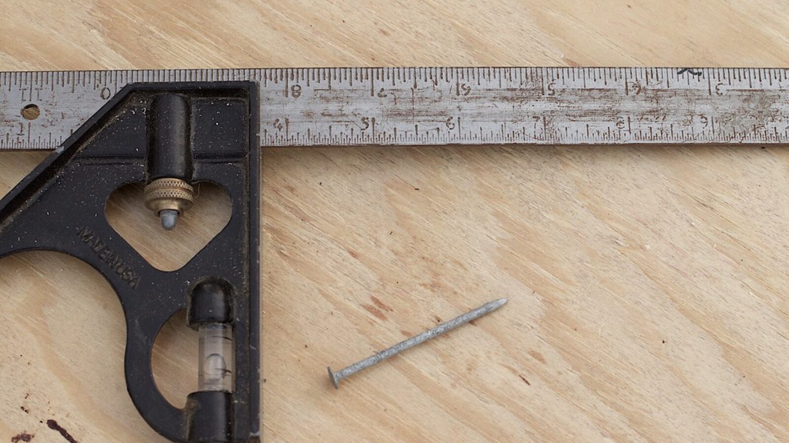 Carpenter's combination square and nail on timber — careful measure and fixings on every fencing job